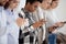 Diverse young people standing in row using smartphones