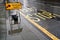 Diverted traffic black and yellow sign on wet pavement, next to road with Bus Stop text, lights reflect in rain covered asphalt