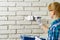 DIY wall repairing, Woman painting a white brick wall with a paint brush