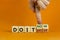 Do it now symbol. Businessman hand turns cubes and changes words `do it later` to `do it now`. Beautiful orange background.