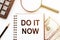 DO IT NOW text written in a notepad with pencil, magnifier, money and calculator around