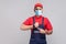 We do ontime. Young man with surgical medical mask in blue overall and red t-shirt standing and showing time on his wrist watch