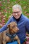 Doberman mix dog sitting in blond womanâ€™s lap, outside on green lawn covered in red fall leaves