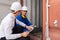 Dock manager and engineer worker in safety helmet sitting in front of container in shipping yard and discuss. Import and export