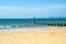 Dock pilings on a sandy beach, blue ocean and yellow sand, sunny