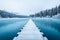 A dock with wooden path on a lake with snowy forest landscape. Beautiful winter background, white clouds in the sky and calm blue