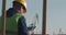 A Dockworker With A Beard In A Yellow Helmet, Works With A Tablet PC In The Seaport Against The Background Of Cranes. The Foreman