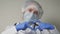 A doctor in a blue mask and gloves smiles and shows his heart, a professional cardiologist in a health clinic, an