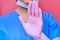 A doctor in a blue uniform on a pink background shows a stop gesture with his hand. Medic in a protective gloves with a sign stop