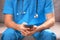 A doctor in a blue uniform with a stethoscope around his neck is sitting on a sofa with a phone in his hands