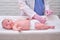 The doctor cuts the toenails of a newborn baby. A nurse in uniform with scissors for the hygiene of the child legs and feet