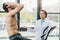doctor with digital tablet gesturing near shirtless sportsman during endurance test in gym.