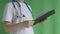 A doctor without a face signs papers on a tablet on a green background, monochrome