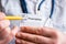 Doctor in foreground holding sample of prescription or recipe for drug, other hand indicates designation of prescription medicatio