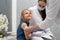 The doctor is getting ready to vaccinate a little girl. A young nurse sits next to the child to make the child feel safe