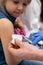 The doctor is getting ready to vaccinate a little girl. A young nurse sits next to the child to make the child feel safe