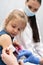 The doctor is getting ready to vaccinate a little girl. A young nurse sits next to the child to make the child feel safe