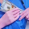 A doctor hides us dollars in a uniform pocket. Medic holds a salary in cash, close up