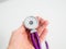 Doctor holding in hand round detail of purple stethoscope on white background. Close-up