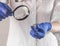 Doctor holding pill and magnifying glass in fingers. Scientist hand closeup studying pharmacology concept