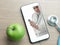 Doctor holding stethoscope on smartphone screen, and green apple on table, doctor online concept, online medical communication and