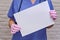 Doctor holds an empty blank sheet of paper, copy space for the inscription. Woman nurse in a blue uniform with a white sheet,