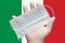 Doctor holds medical face mask in hand in white gloves on background colors flag of Italy. Concept pandemic insurance coronavirus