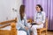 Doctor in hospital writing prescription to patient. Two women sitting on sofa and looking on clipboard