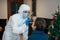 Doctor laboratory assistant in protective suit takes swab from patient nose, at home during Christmas