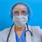 The doctor looks scared in protective glasses and a medical mask, blue background. Nurse with wide-open eyes, close-up portrait