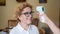 Doctor measures temperature with non-contact infrared thermometer smiling elderly woman at home