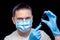 Doctor in a medical mask and sterile blue gloves holds in his hands a syringe.