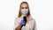 Doctor or nurse pointing sensor thermometer on camera wearing protective mask white medical hospital robe. Young blond