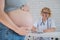 Doctor obstetrician gynecologist at his desk in the background. Close-up of a pregnant woman's belly.