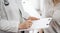 Doctor and patient view. Female physician is filling up a medical records form near a woman having a medical examination