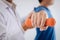 Doctor physiotherapist assisting a male patient while giving exercising treatment on stretching his arm with dumbbell in the