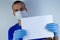 Doctor in a protective mask on a blue background. holds a document a sheet of white paper in gloves.copyspace for text