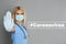 Doctor in protective mask showing stop gesture near hashtag Coronavirus on grey background