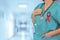 Doctor with red ribbon AIDS, HIV on blurred background of hospital hall. Medical web sites with copy space. Health care banner