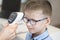 Doctor`s hand measures the temperature of the boy in a blue shirt and glasses using an electronic infrared thermometer.