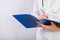 Doctor`s hands in a white coat hold a folder and fill out a medical document close-up isolated on a white background.