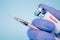 Doctor or scientist holding vial dose of common vaccine with syringe against blue background with copy space - prevention