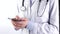 Doctor standing, holding and typing on mobile phone, wearing stethoscope, white