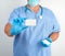 Doctor in sterile latex gloves and blue uniform holds a blank white business card