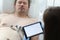 Doctor taking cardiogram to sick patient man on digital tablet in clinic closeup