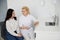 Doctor talking with patient during medical consultation at office. Young female dentist showing laptop patient at desk in clinic