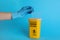 Doctor throwing used syringe needle into sharps container on light blue background, closeup