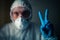 A doctor with a tired look in a respirator, glasses and a bacteriological protection suit shows a victory sign with a