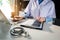 Doctor using digital technology laptop for Output Device and writing a patient report on the office desk.