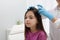Doctor using lice treatment spray on little girl`s hair indoors